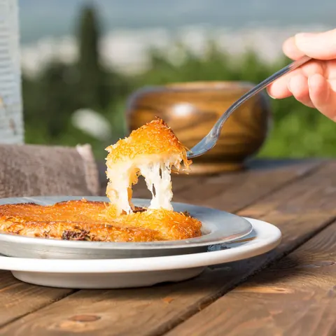 Lifting a forkful of cheese kunafa at an outdoor table