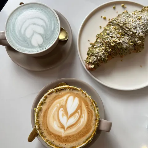 A pistachio latte, a blue latte and a pistachio croissant from above