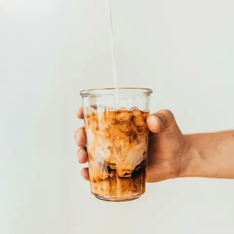Milk poured into a glass of iced coffee