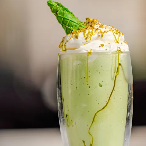 A pistachio milkshake with whipped cream and a green cone