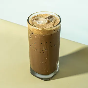 A glass of iced kopi on a sunny table