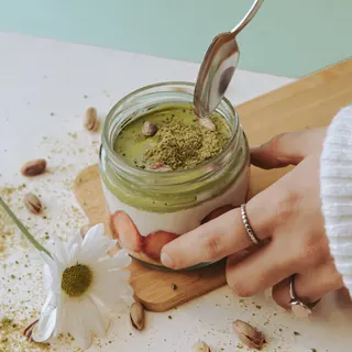 A jar of pistachio milk pudding with a spoon