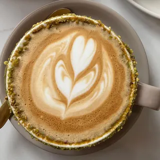 A pistachio latte with latte art and a pistachio rim