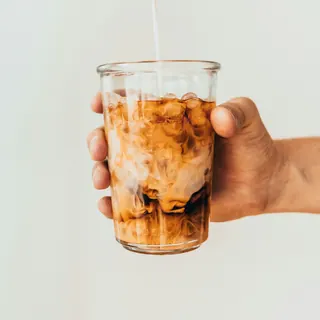 Milk being poured into a glass of iced coffee
