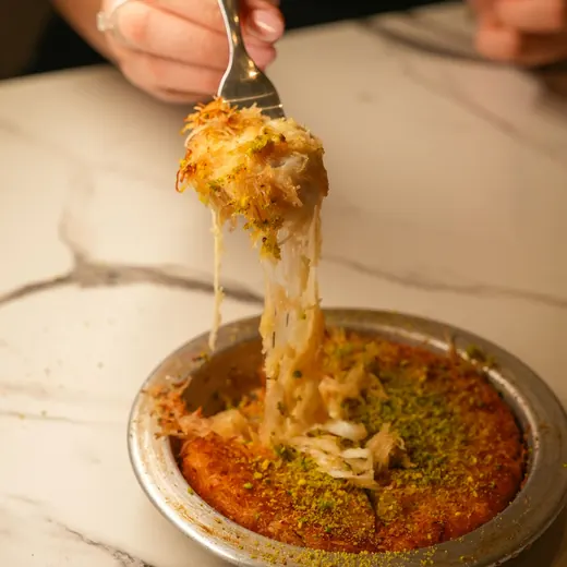 A fork pulling up a piece of cheese kunafa with long strands of cheese