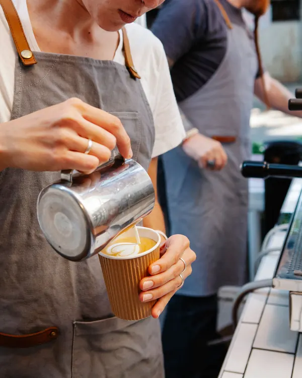 A barista pouring latte art into a takeaway cup